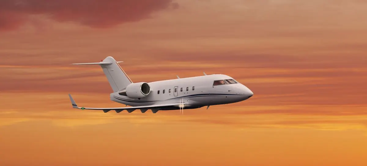 A private jet in flight against an orange sunset sky